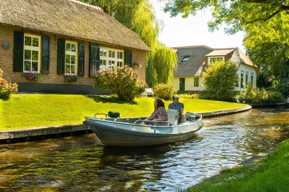 Gasten varen in een sloep langs rietgedekte huizen in Giethoorn